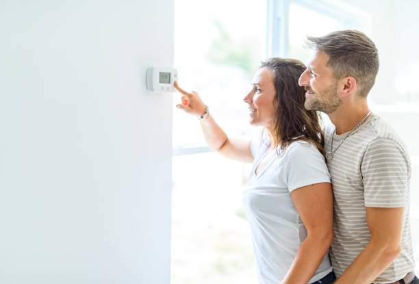 istock Smiling couple Adjusting Thermostat On Home Heating System 2187142944