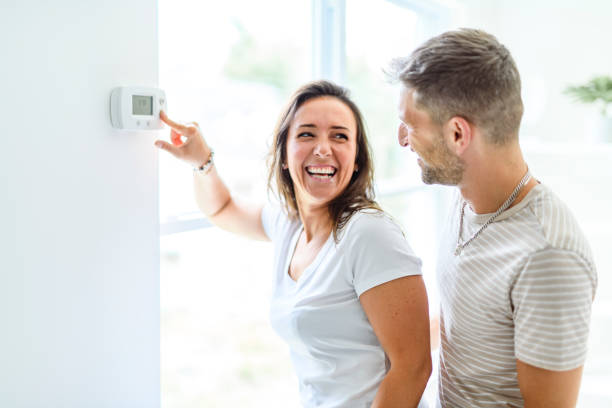 Smiling couple Adjusting Thermostat On Home Heating System