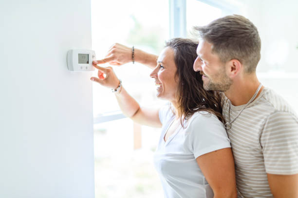 istock Smiling couple Adjusting Thermostat On Home Heating System 2187142959