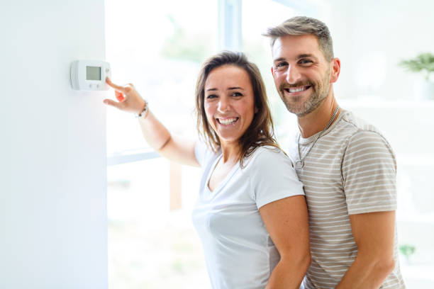 istock Smiling couple Adjusting Thermostat On Home Heating System 2187142981
