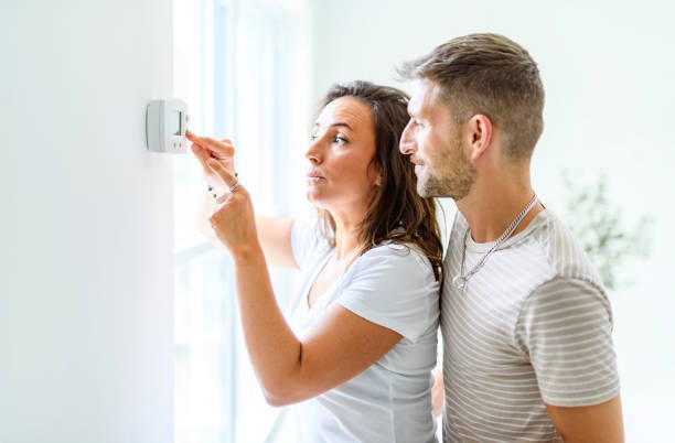istock Smiling couple Adjusting Thermostat On Home Heating System 2187142992
