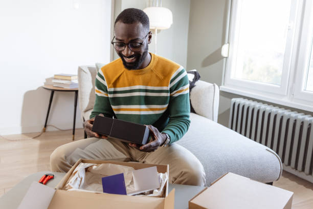 istock Man happily unboxing a product while sitting in a bright living room 2187145749