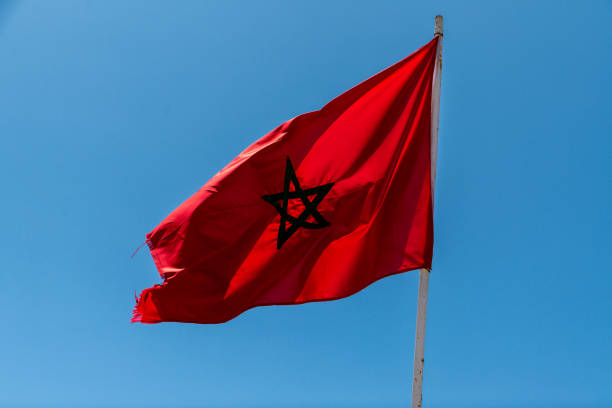 Moroccan flag fluttering in the wind with a red background and green pentagram, captured against a blue sky.