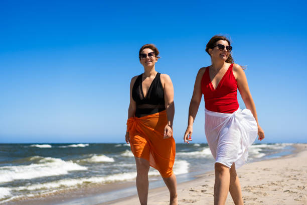 istock Two beautiful mature women walking on sandy beach. 2187147959