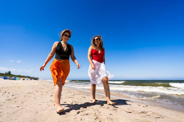 istock Two beautiful mature women walking on sandy beach. 2187147976