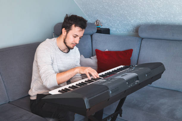 istock young man sitting on a comfortable couch while playing a digital keyboard, surrounded by cozy pillows and a calm home environment. A moment of creativity and focus 2187148080