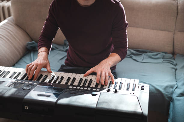 istock Man playing a digital keyboard in a relaxed home setting, seated on a sofa with natural light streaming in, capturing a peaceful and focused musical moment 2187148277