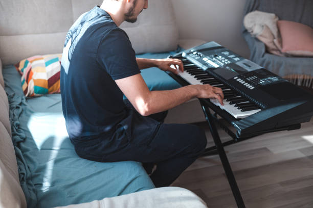 istock Man playing a digital keyboard in a relaxed home setting, seated on a sofa with natural light streaming in, capturing a peaceful and focused musical moment 2187148357