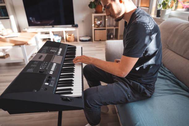 istock Man focused on playing a digital keyboard in a sunlit living room, surrounded by modern decor and warm natural light, creating a serene and inspiring atmosphere 2187148398