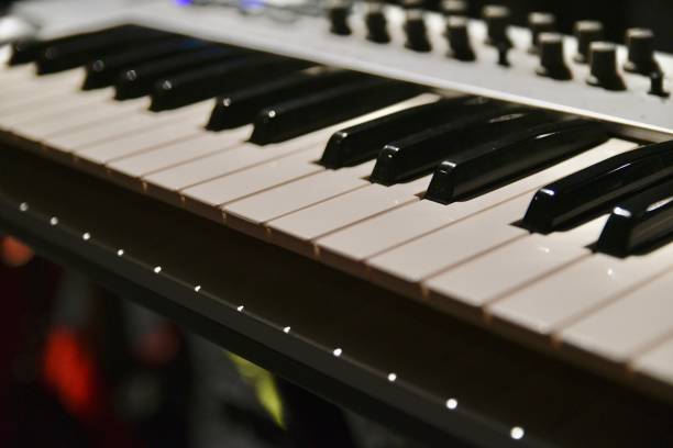 A detailed shot of a professional electric keyboard on stage, illuminated by stage lights. The close-up highlights the keyboard’s keys and controls, with a focus on the polished surfaces and vibrant lighting. The image captures the energy and anticipation of a live performance, offering a glimpse into the musician’s tool of creation in a dynamic and immersive setting. This composition evokes the rhythm and pulse of a live musical experience.