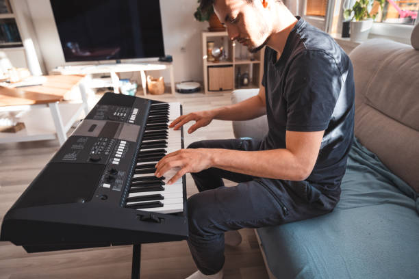 istock Man focused on playing a digital keyboard in a sunlit living room, surrounded by modern decor and warm natural light, creating a serene and inspiring atmosphere 2187148402