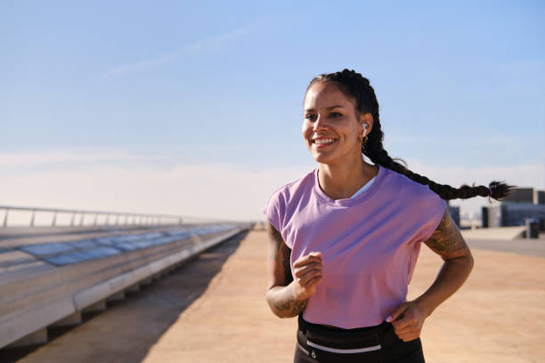 front view portrait of a fit and carefree Latino female with big smile running on a boardwalk in Barcelona city on a sunny day. sport and healthy lifestyle concept stock photo