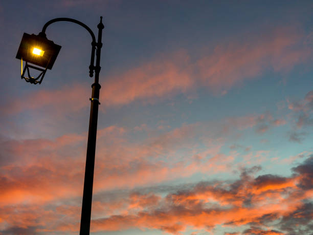 Close up of a street lamp with a winter sky background, with clouds and warm colors of sunset