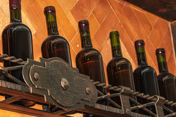 Dark wine bottles sit neatly on a metal shelf. Warm terracotta tiles at the back create a rustic and cozy atmosphere. The vintage aesthetic evokes a sophisticated atmosphere, perfect for wine lovers.