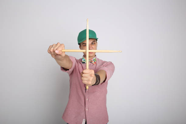 A young male drummer holding drumsticks on a neutral, isolated studio background. Concept of modern music, drumming education, a drummer career in a band, creative hobbies, and artistic professions. High quality photo