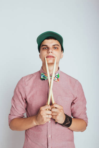A young male drummer holding drumsticks on a neutral, isolated studio background. Concept of modern music, drumming education, a drummer career in a band, creative hobbies, and artistic professions. High quality photo