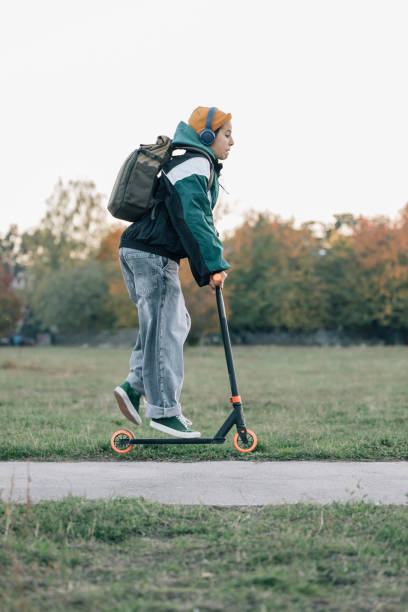 istock Young student going to school riding a scooter in the park 2187165787