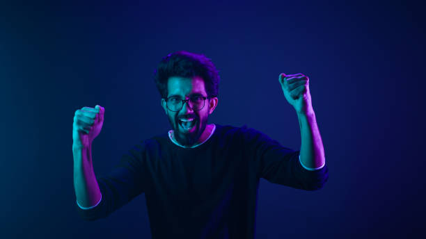 istock Happy Indian man in ultraviolet neon studio background champion coding achievement level up celebrating winning championship fan support victory supporter cheering competition excited goal spectator 2187166406