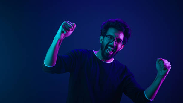 istock Happy Indian man in ultraviolet neon studio background champion coding achievement level up celebrating winning championship fan support victory supporter cheering competition excited goal spectator 2187169046
