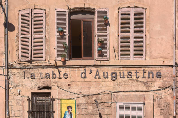Marseille. France  - November 27,2024: A vintage French building with open and closed shutters, flower pots, and the sign La table d'Augustine. Great for themes of old-world charm and quaint architecture.
