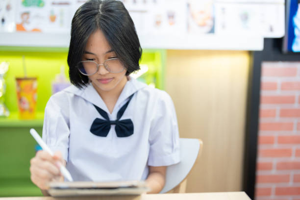 istock A diligent student in a school uniform sits in a colorful cafe, completely absorbed in writing on her tablet, demonstrating her focus, discipline, and dedication to academic success. 2187174314