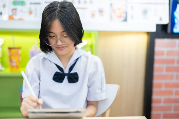 istock With her glasses slightly slipping down her nose, she leans over her tablet, fully immersed in her studies, a perfect example of determination and hard work in a cozy setting. 2187174315