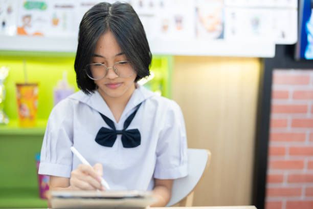 A young student, dressed neatly in her uniform, concentrates deeply on her tablet, showcasing her unwavering focus while the warm ambiance of the cafe surrounds her.