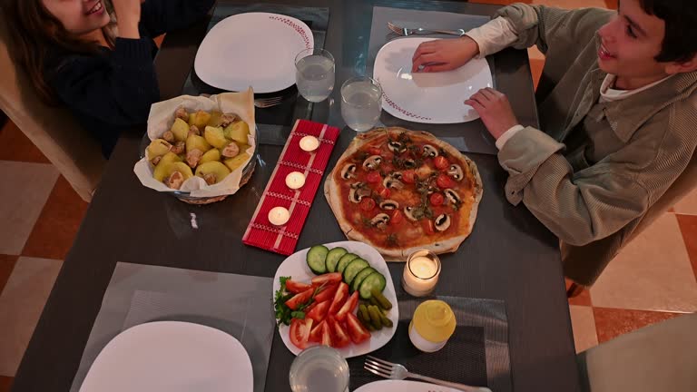 Cozy family dinner table setting with homemade pizza, fresh vegetables, and candles creating a warm inviting atmosphere