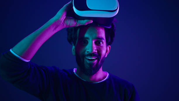 istock Arabian man take off VR glasses excited smile amazed with metaverse virtual reality cyberspace Indian guy with 3d goggles helmet happy wow reaction after play game meta universe neon ultraviolet space 2187179600