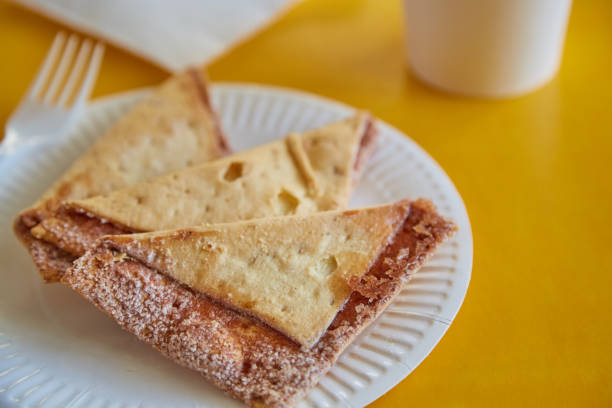 istock Freshly baked tortilla chips with sugar and cinnamon on a paper plate next to a glass, fork, and napkins against a yellow background, close-up. 2187182682