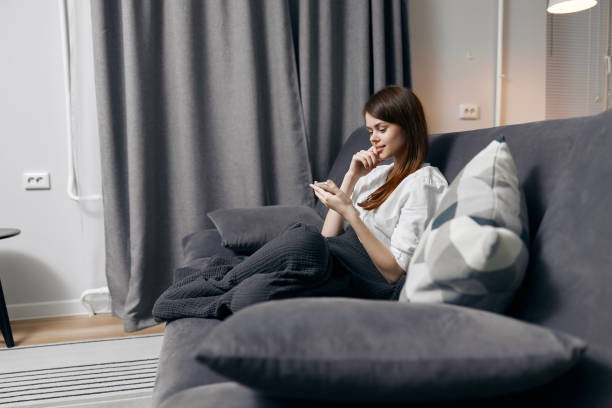 istock woman covered with a blanket sits on the couch with a mobile phone in her hand side view 2187184164