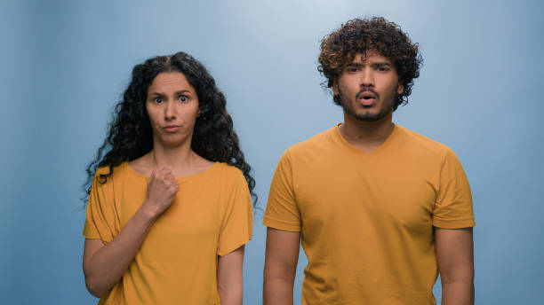 istock Multiracial shocked scared afraid couple amazed shocked Hispanic woman hiding behind Indian man astonishment wonder scare terrible horror ugly reaction blue studio background shock astonish fright 2187192512