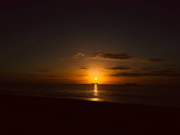 Serene sunset casting warm hues over a calm sea, with the tranquil water reflecting the rich, golden light in a dramatic and peaceful dark-toned scene.