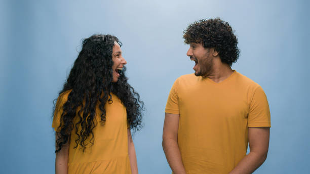 istock Portrait in blue background studio diverse multiracial couple looking at each other amazed surprised laughing open mouth laugh answer different opinions woman girl no man guy yes disagree discrepancy 2187195976
