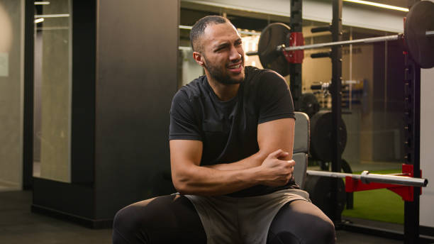 istock African American man guy in gym doing sport exercise with dumb-bell curl biceps workout sportsman athlete lifting up heavy dumbbell weights feel sharp pain in joint hand elbow painful injury trauma 2187201055