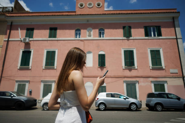 Strolling through Rome, a female tourist checking her phone against a backdrop of historic buildings and vibrant street life, rear view