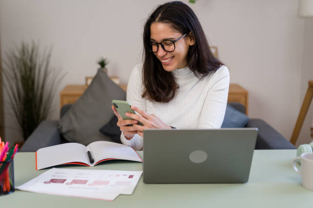istock businesswoman using smartphone and smiling while working from home 2187202570