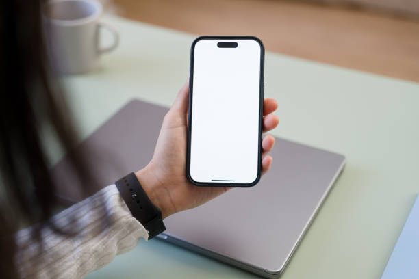 Woman holding smartphone with blank screen at office desk