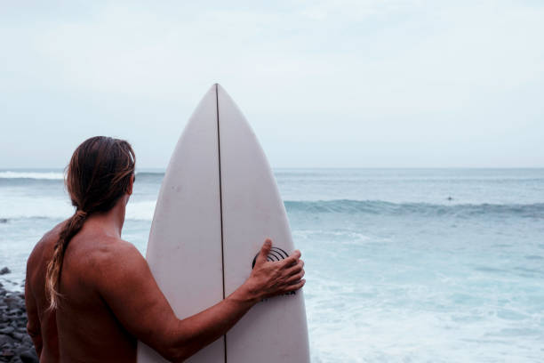 istock A Long-Haired Man Holding a Surfboard, Standing Confidently on the Beach. 2187203149