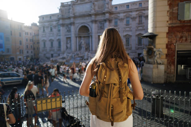 Rear view of woman with backpack while looking at fountain di Trevi in Rome