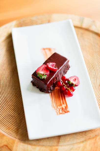 Delicious chocolate dessert beautifully garnished with fresh strawberries and red currants, presented on a white plate, offering an enticing and sophisticated gastronomic delight for gourmet dining