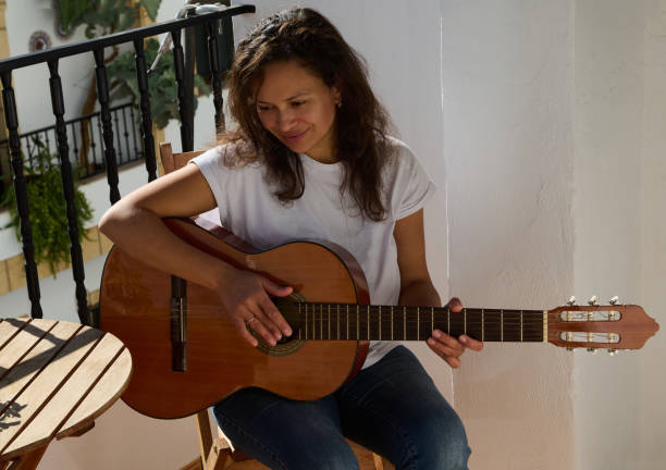 istock Woman playing guitar on a sunny balcony with calm expression 2187208234