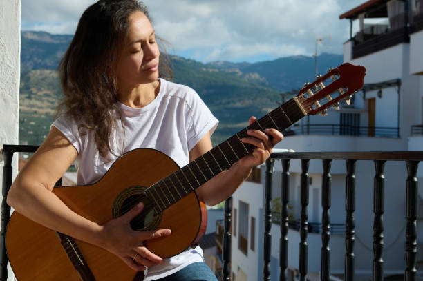 istock Woman playing guitar on sunny balcony with mountain backdrop 2187208242