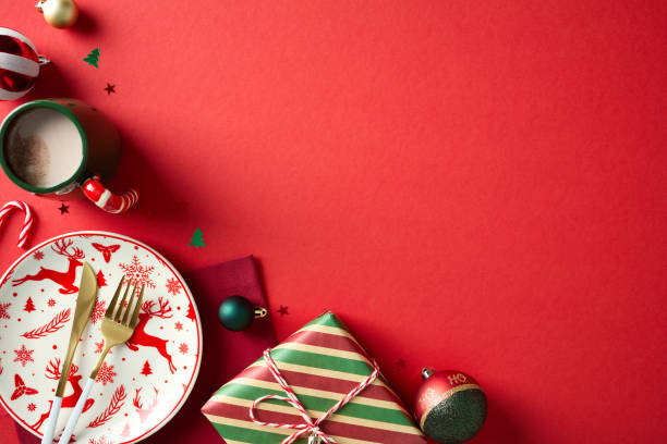 istock Christmas table setting with plate, golden cutlery, decorations, baubles, cacao cup, candy canes on red background. Flat lay, top view, copy space. 2187210477