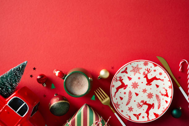 istock Festive table setting with plate in Christmas plate, cacao cup, truck with Christmas tree, baubles on red background. Top view. 2187210518