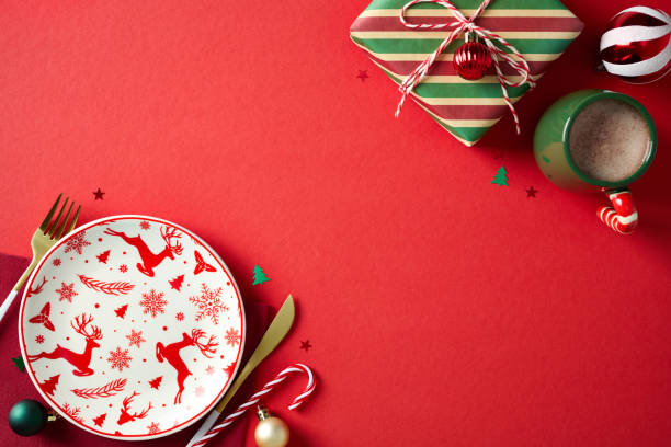 istock Christmas dinner concept. Xmas table top view with empty plate, cutlery, vintage gift, cacao cup, baubles on red background. Flat lay, top view. 2187210731