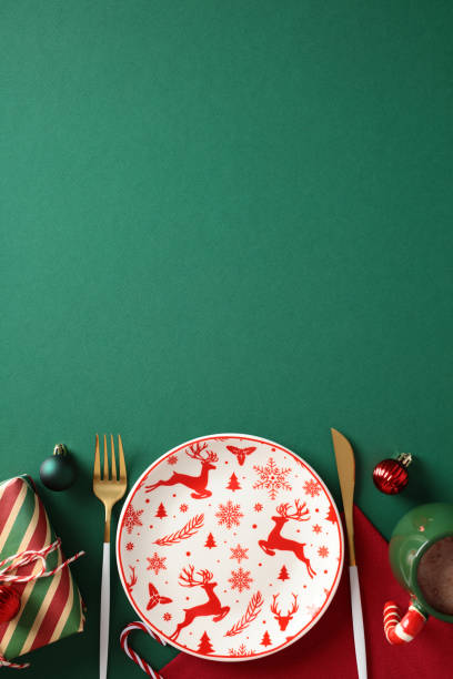istock Christmas table setting with empty reindeer plate, gold cutlery, wrapped gift, and ornaments on a green background 2187211068
