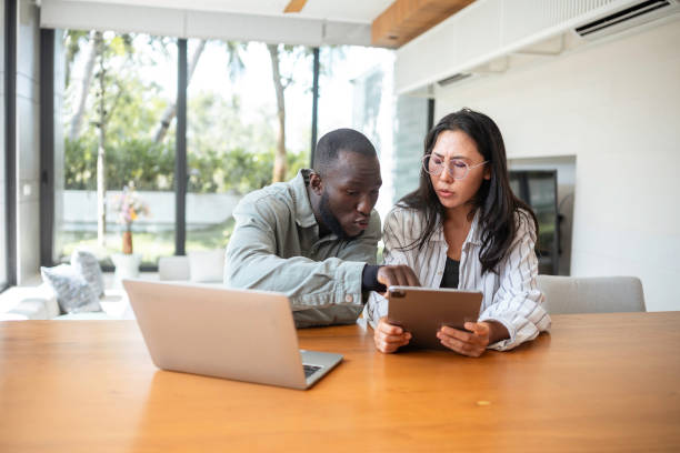 istock Black Man and Asian Woman Collaborating with Tech at Home 2187217271