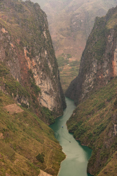 This captivating photograph showcases the dramatic landscape of Tu San Gorge in Ha Giang, Vietnam, with the Nho Que River winding its way through the steep, towering cliffs