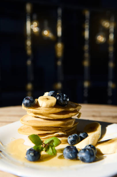 Stack of pancakes with blueberries and bananas drenched in syrup